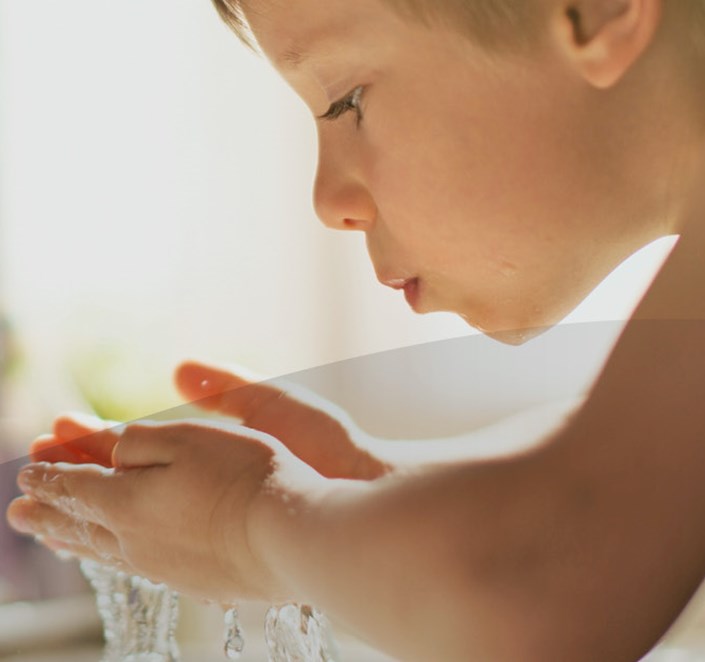 Dreng drikker vand af vandhane indendørs.