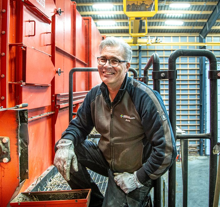 Medarbejder foran stor maskine, som håndtere halm til fjernvarme